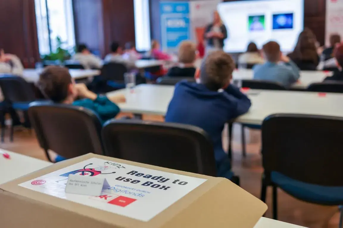 Ready-to-use-Box mit KIDZ, OCG und AK Wien Logos, im Hintergrund Zemanek Saal/Workshop