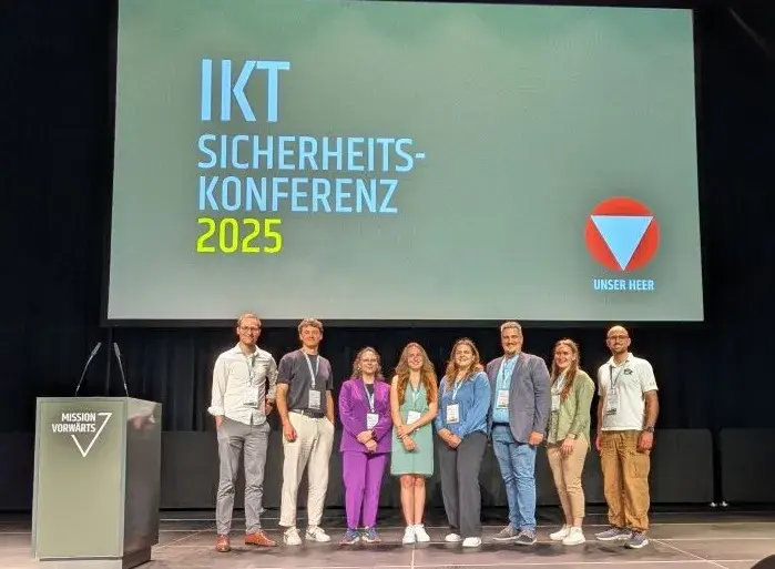 Acht Personen - die Young Researcher - auf einer Bühne, im Hintergrund Schriftzug IKT Sicherheitskonferenz 2025 und das Logo des Bundesheeres