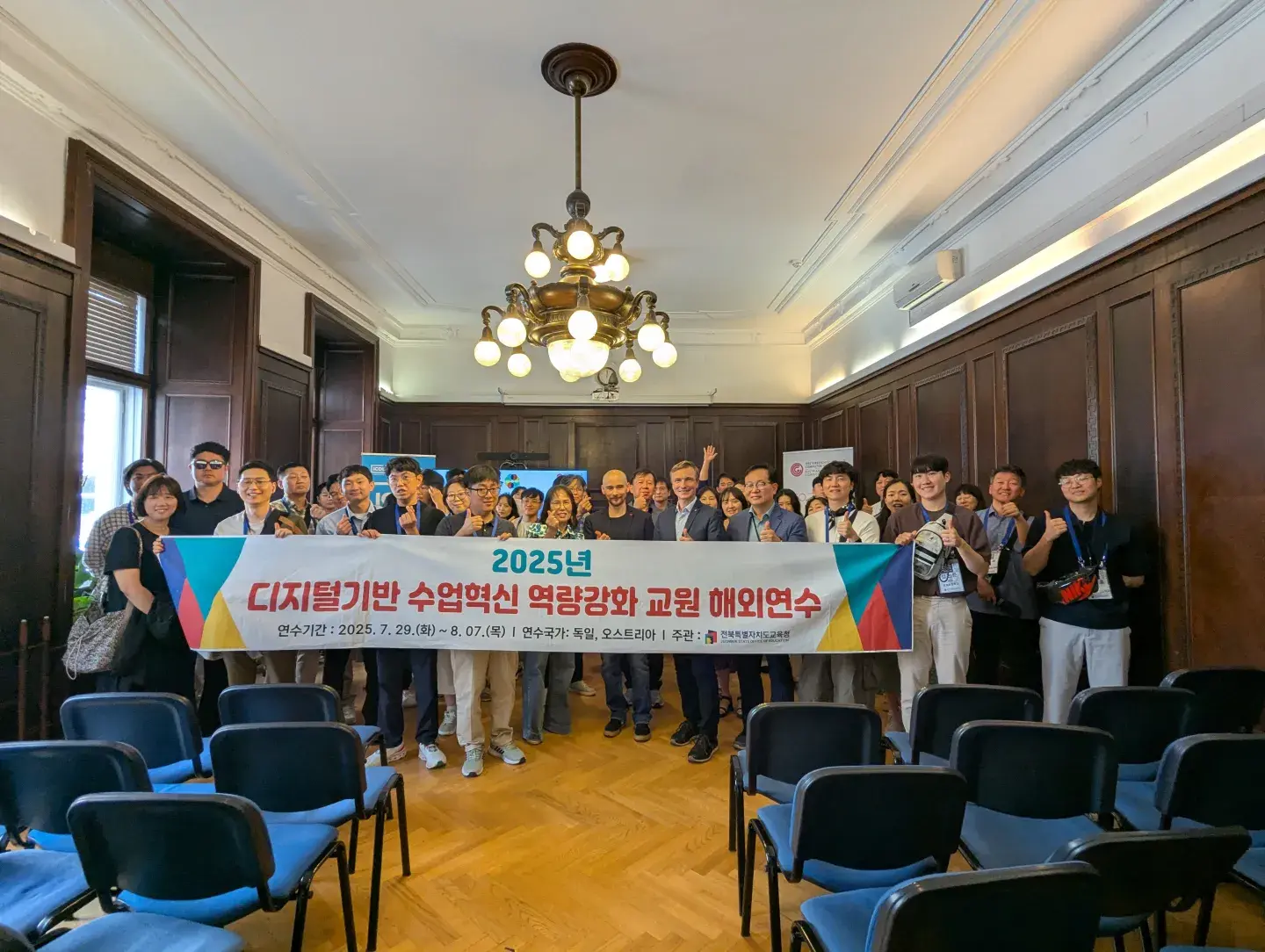 Gruppenfoto vom Besuch der Delegation aus Südkorea mit Ronald Bieber und Martin Kandlhofer im Heinz Zemanek Saal in der OCG. Ca. 50 Personen von der Delegation, sie halten ein Transparent mit koreanischer Schrift.