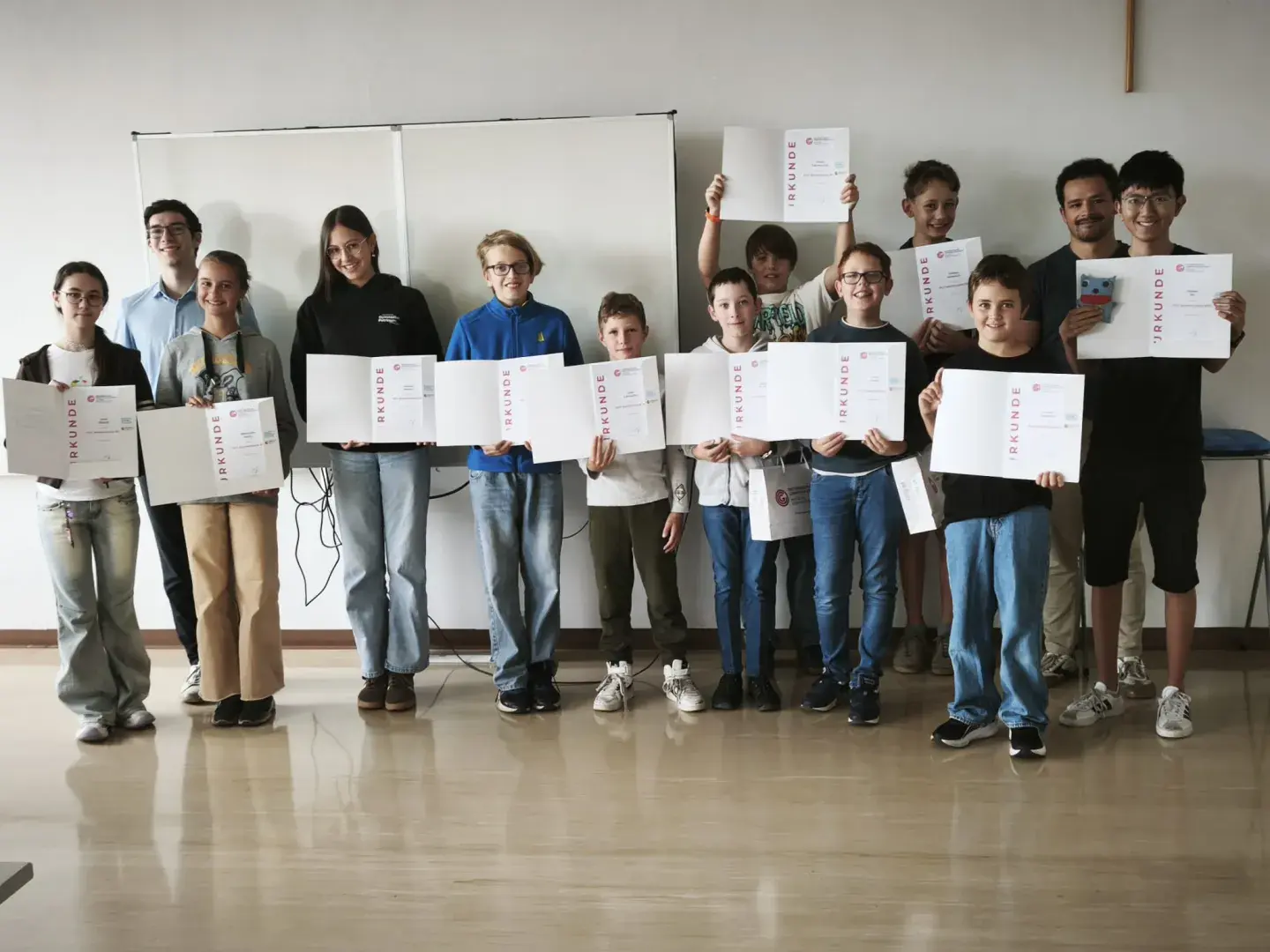 Gruppenfoto der elf 10-15-Jährigen TeilnehmerInnen mit den Abschlussurkunden des OCG Sommercamps Linz und den Camp-Betreuern Elias Wiesenhofer und Liam Baumann.