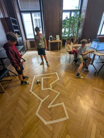 Roboter wird durch eine Rennstrecke gesteuert. Vier Kinder beobachten das Ergebnis ihrer Programmierung. 