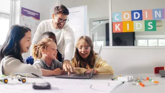 Vier Mädchen und ein Lehrer vor einem Laptop