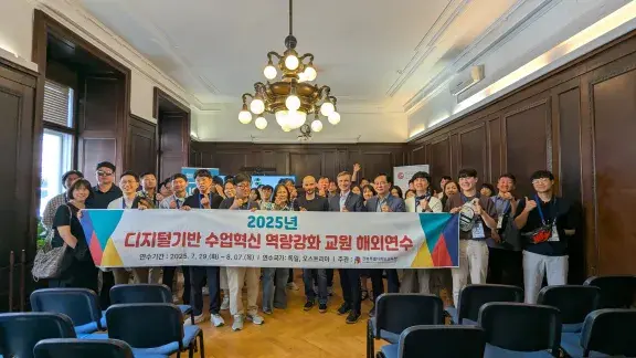 Gruppenfoto vom Besuch der Delegation aus Südkorea mit Ronald Bieber und Martin Kandlhofer im Heinz Zemanek Saal in der OCG. Ca. 50 Personen von der Delegation, sie halten ein Transparent mit koreanischer Schrift.