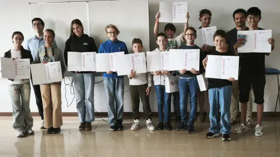 Gruppenfoto der elf 10-15-Jährigen TeilnehmerInnen mit den Abschlussurkunden des OCG Sommercamps Linz und den Camp-Betreuern Elias Wiesenhofer und Liam Baumann.